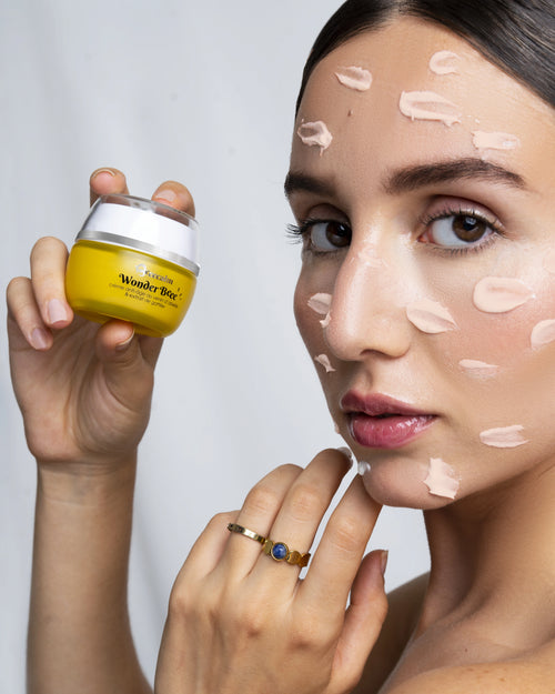 Femme tenant un pot de WonderBeee, avec produit sur le visage.
